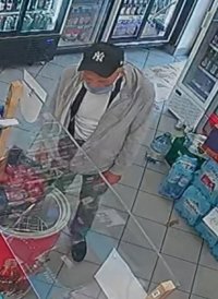 wizerunek sprawcy kradzieży mężczyzna w czapce z daszkiem koloru czarnego, na twarz ma  maseczkę, ubrany w bluzę  koloru szarego , pod nia biały t- shirt, spodnie ciemne, stoi przy ladzie sklepowej