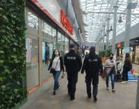 w galerii handlowej widoczni są tyłem dwaj umundurowani policjanci, kilka osób w maseczkach znajduje się na holu galerii, z lewej strony witryna sklepowa