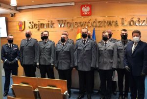 na zdjęciu, w sali urzędu marszałkowskiego stoją w dwuszeregu umundurowani policjanci, obok nich stoi marszałek województwa łódzkiego