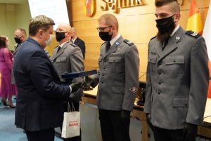 na zdjęciu widoczni są umundurowani policjanci oraz marszałek województwa łódzkiego, który wręcza nagrodę pamiątkową jednemu z funkcjonariuszy