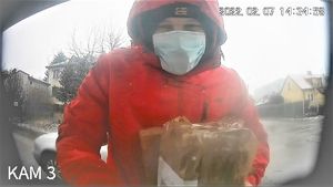 wizerunek mężczyzny w czerwonej kurtce z kapturem na głowie i maseczką na twarzy który trzyma w rękach przesyłkę