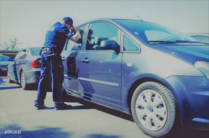 Umundurowany policjant zagląda przez szybę do samochodu.