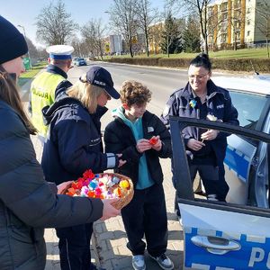Policyjna akcja z okazji Dnia kobiet. Policjanci z dziećmi rozdają kwiatki kobietom.