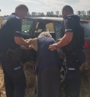 policjanci pomagają starszej kobiecie wsiąść do radiowozu