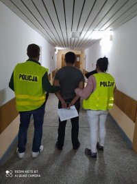 na korytarzu Komendy dwóch policjantów prowadzi zatrzymanego, który na rękach ma złżone kajdanki