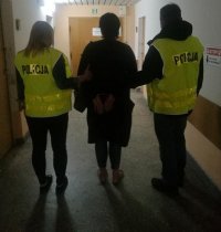 dwóch policjantów  prowadzi oszustkę, która ma założone kajdanki na ręce trzymane z tylu