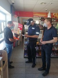 w sklepie stoi policjant, który dokonuje zapisek w notatniku,  obok członek komisji, sprzedawca trzyma w reku wręczone mu plakaty