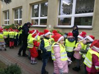 przed budynkiem Przedszkola nr 15 w Sieradzu grupa kilkudziesięciu dzieci wspólnie z policjantami dekoruje drzewka elementami odblaskowymi. Policjanci ubrani są w granatowe mundury na głowach maja czapki mikołaja, dzieci mają założone kamizelki odblaskowe, na głowach czapki mikołaja,