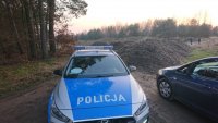 w pobliżu kompleksu leśnego ujawniono hałdy z nielegalnymi odpadami, widać stojący oznakowany radiowóz policyjny oraz drugi samochód, po lewej stronie widać drzewa
