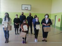 Na sali gimnastycznej szkoły stoją laureaci konkursu z dyplomami w dłoniach, nauczycielki, za nimi dyrektorka szkoły oraz dwóch umundurowanych policjantów, wszyscy mają maseczki na twarzy
