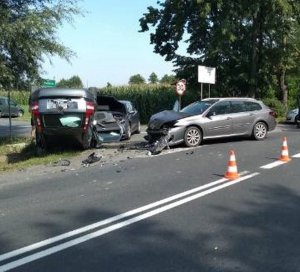 na obrazku widoczne jest skrzyżowanie, na którym znajdują się trzy uszkodzone samochody osobowe; jeden z pojazdów leży na dachu a wokół rozrzucone są części samochodowe;