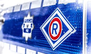 na niebieskim tle widoczna jest policyjna odznaka oraz logo ruchu drogowego- litera "R" w czerwonej obwódce umieszczona w rombie z biała obwódką