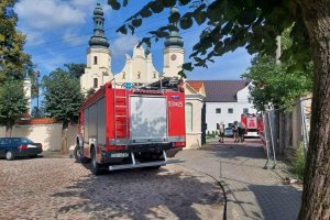 Przed bramą klasztoru stoi wóz bojowy straży pożarnej, samochody osobowe