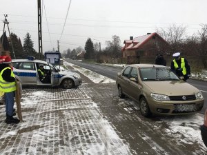 Dzieci wspólnie z policjantami przeprowadzają kontrole drogowe kierowców i wręczają woreczki  z ziemią  lub uśmiechnięte zawieszki,