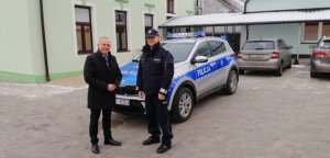 na zdjęciu widoczni są dwaj mężczyźni, jeden to umundurowany funkcjonariusz policji, stojący na tle radiowozu policyjnego