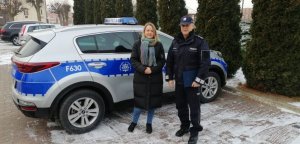 na zdjęciu widoczna jest kobieta i umundurowany funkcjonariusz policji, stojący obok policyjnego radiowozu