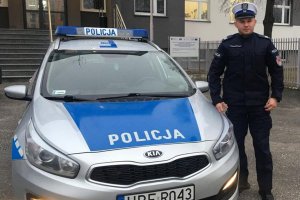 przed budynkiem komendy obok oznakowanego radiowozu stoi umundurowany policjant