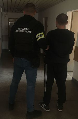 policjant w kamizelce z napisem Wydział Kryminalny prowadzi zatrzymanego