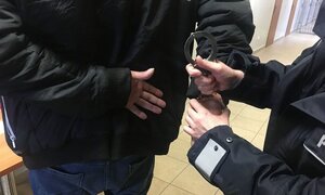 w areszcie umundurowany policjant zakłada kajdanki zatrzymanemu