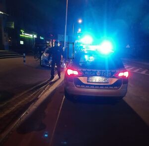 miejsce wypadku z udziałem rowerzysty przed oznakowanym radiowozem stoi umundurowany policjant i kilka osób