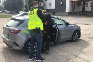 policjant w kamizelce odblaskowej wprowadza nieoznakowanego radiowozu zatrzymanego który ma założone na rękach kajdanki