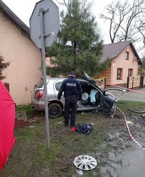 miejsce wypadku śmiertelnego rozbity samochód z uderzył w ogrodzenie posesji, przy samochodzie umundurowany policjant z lewej strony czerwony parawan