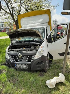 miejsce kolizji widać dostawczy biały samochód z uszkodzonym przodem obok policjantów i strażaków wykonujących czynności