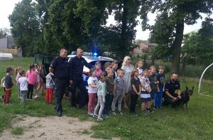 umundurowani policjanci uczestniczą w spotkaniu z dziećmi, w tle radiowóz policyjny