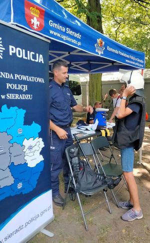 podczas pikniku przy namiocie policyjnym chłopiec przymierza elementy wyposażenia do służby obok stoi umundurowany policjant,