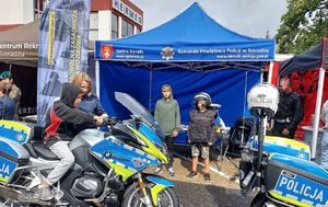 pod niebieskim namiotem stoisko policyjne na Jarmarku Powiatowym, przed namiotem stoją oznakowane motocykle, na jednym z nim siedzi dziecko obok stoją policjanci