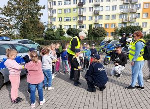 umundurowanych policjantka  i policjant rozdaje dzieciom kamizelki odblaskowe, obok  policyjny radiowóz