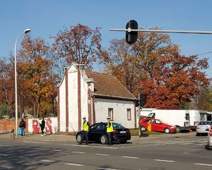 umundurowani policjanci stoją na skrzyżowaniu przed cmentarzem przy nieoznakowanym radiowozem,