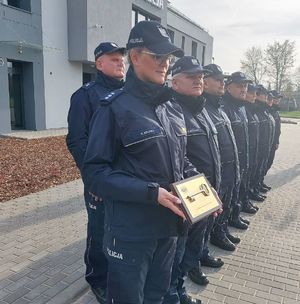 Uroczystość otwarcia nowej siedziby Komisariatu Policji w Warcie – Komendant KP trzyma tabliczkę z kluczem, obok stoją policjanci przekazuje symboliczny klucz Komendantowi Komisariatu Policji w Warcie, po prawej stronie namiot gdzie stoją zaproszeni goście