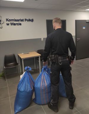 na korytarzu komisariatu umundurowany policjant stoi przy workach w nielegalnym tytoniem