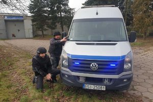 ćwiczenia w zakładzie karnym z udziałem policji służby więziennej i staży pożarnej, funkcjonariusze z bronią w ręku , klęczą przy oznakowanym samochodzie