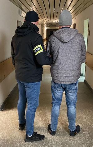 na korytarzu komendy  policjant w opaską na ramieniu z napisem POLICJA prowadzi zatrzymanego