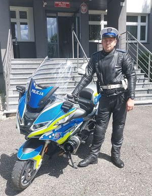 Przed budynkiem komendy obok policyjnego motocykla stoi umundurowany policjant.