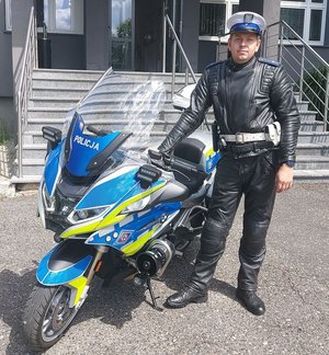 Przed budynkiem komendy przy motocyklu policyjnym stoi umundurowany policjant.