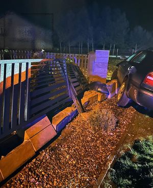 Uszkodzone ogrodzenie posesji , obok stoi uszkodzony samochód osobowy.