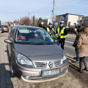 W samochodzie siedzi mężczyzna i kobieta, policjanci stoją przy samochodzie.