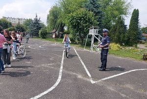 Umundurowany policjant przeprowadza egzamin uczniów klas IV na kartę rowerową na terenie miasteczka ruchu drogowego Szkoły Podstawowej Nr 10 w Sieradzu.