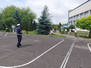 Umundurowany policjant przeprowadza egzamin uczniów klas IV na kartę rowerową na terenie miasteczka ruchu drogowego Szkoły Podstawowej Nr 10 w Sieradzu.