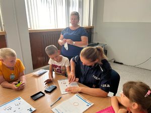 Na zdjęciu policjantka, która trzyma dłonie chłopca skierowane w kierunku kartek papieru.