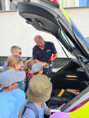 Na zdjęciu policjant prezentuję stojącym wokół niego dzieciom sprzęt policyjny.