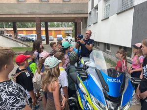 Na zdjęciu widać stojącego funkcjonariusza policji za motocyklem wokół, którego stoją dzieci.