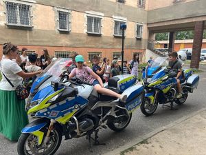 Na zdjęciu widoczne dwa motocykle służbowe policyjne na których siedzą dzieci, tuż za nimi stoją dzieci oraz kobieta.