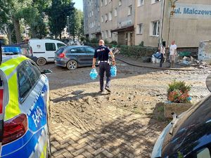 Na zdjęciu widać policjanta niosącego w dłoniach butelki z wodą.