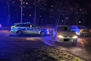 Miejsce zdarzenia drogowego na terenie miasta , pora wieczorna, widać policjantów, oznakowany radiowóz, osobowy samochód.