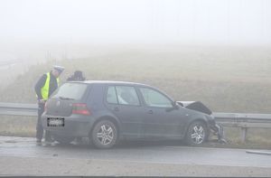 Na poboczu drogi stoi uszkodzony samochód, który uderzył  w barierki ochronne, obok samochodu stoją dwaj umundurowani policjanci.