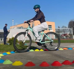 Dziewczynka na rowerze pokonuje tor przeszkód, obok stoi umundurowany policjant.